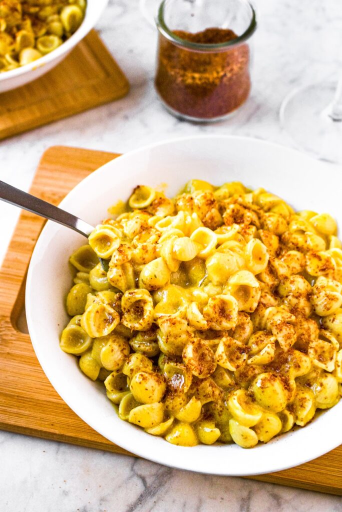 Overhead view of a round white bowl filled with this daiya mac and cheese recipe topped with coconut bacon salt with a spoon pulling some of it out
