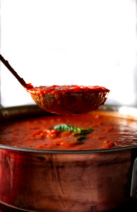 A ladle pulls a cup of marinara sauce out of a large pot