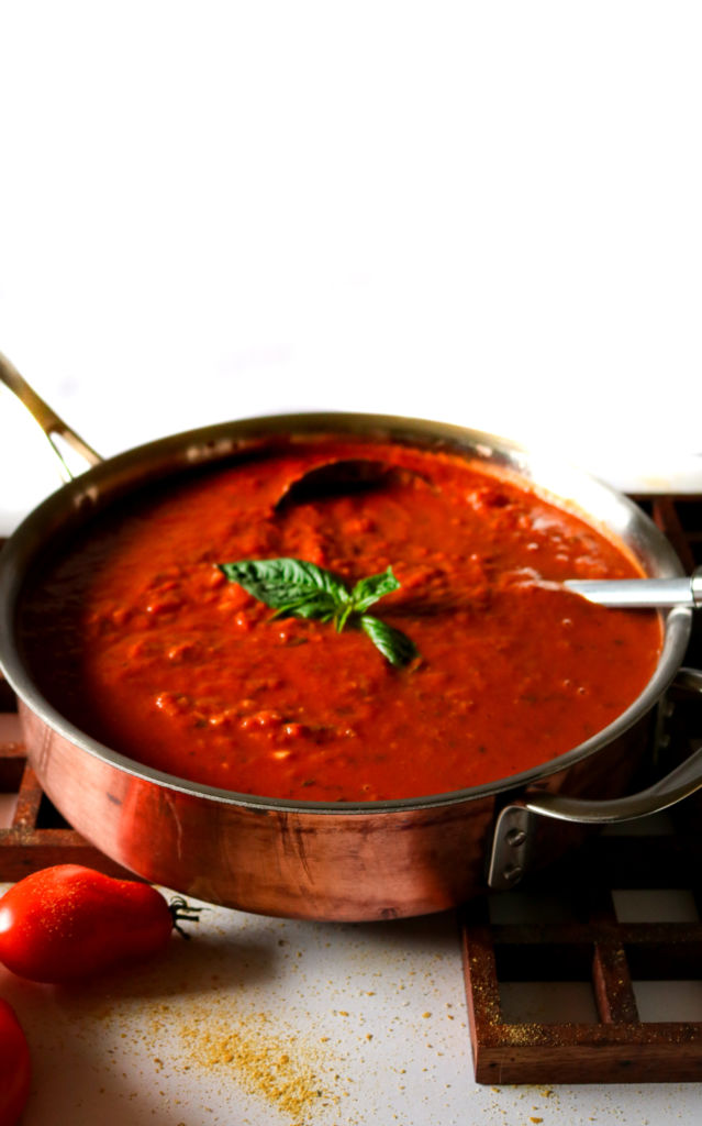 Overhead photo of a large pot of homemade tomato sauce topped with fresh basil