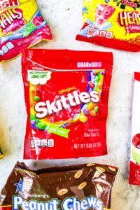 Overhead shot of a bag of accidentally vegan Skittles surrounded by bags of other candies like Swedish Fish, Sour Patch Kids, and Peanut Chews