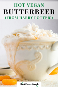Head on shot of a mug of vegan butterbeer with some spilling down the side. There is a swirl of dairy free whipped cream on top of the mug and butterscotch candies surrounding it. Text reads: hot vegan butterbeer from harry potter.
