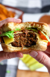 Close up photo of two hands holding a tvp burger with a big bite taken out of it.