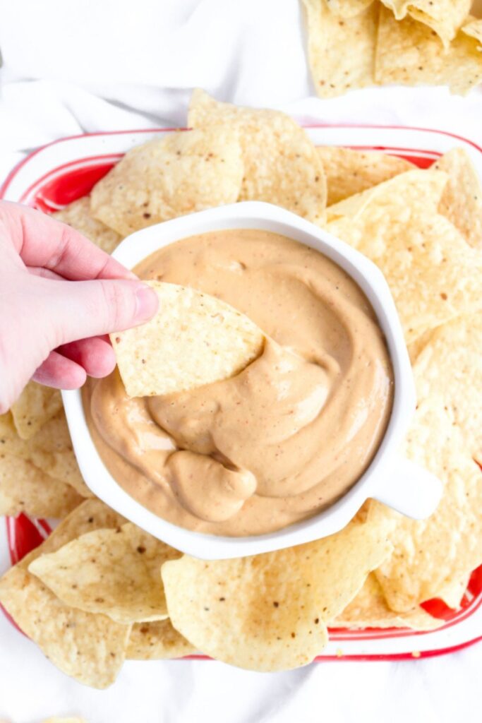 Overhead view of a chip being dipped into a creamy vegan queso sauce in a round white bowl