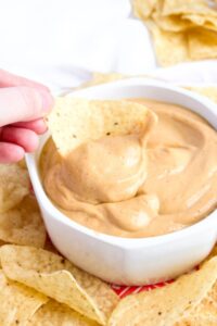 Overhead close up view of a chip being dipped into a creamy vegan queso sauce in a round white bowl