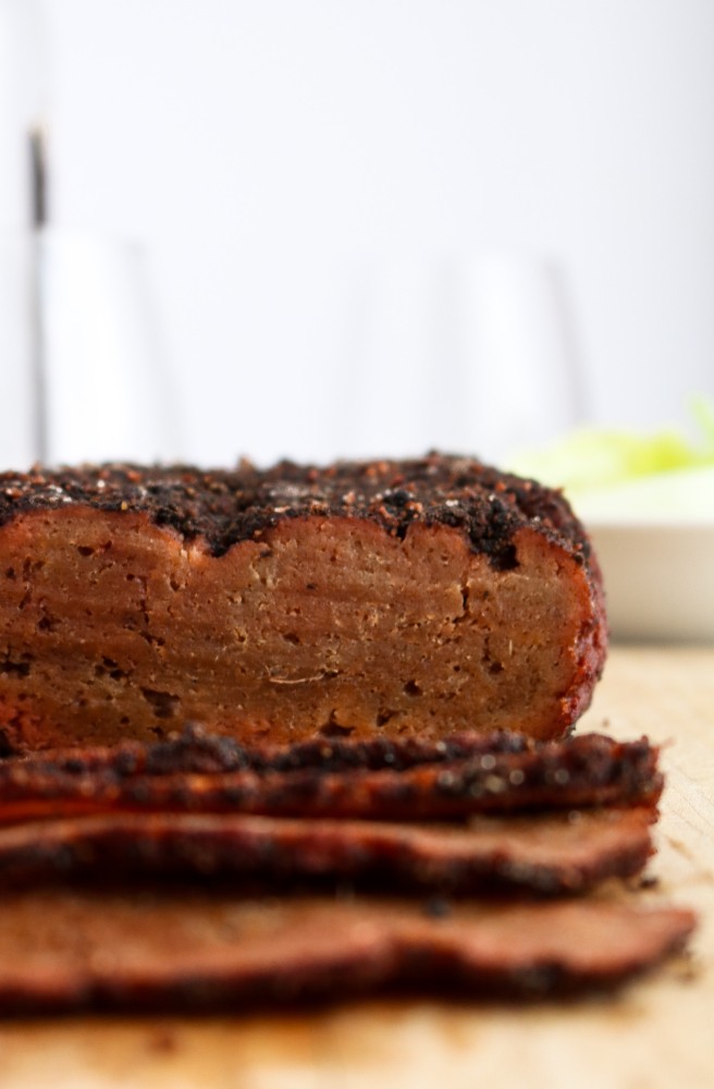 Head on photo of a partially sliced vegan corned beef seitan roast on a wood cutting board