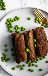 Overhead photo of a pile of vegan seitan sausages on a plate sprinkled with green peas