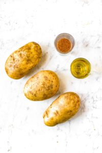 Overhead photo of three potatoes and two small glasses of olive oil and fry seasoning