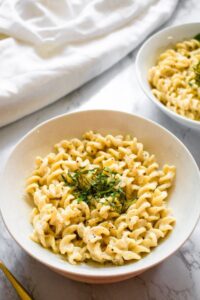 Overhead view of a round white bowl filled with rotini pasta in a creamy vegan garlic sauce topped with shredded fresh green basil