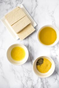 Overhead view of all the ingredients you need to make lemon pepper tofu laid out on a grey marble countertop