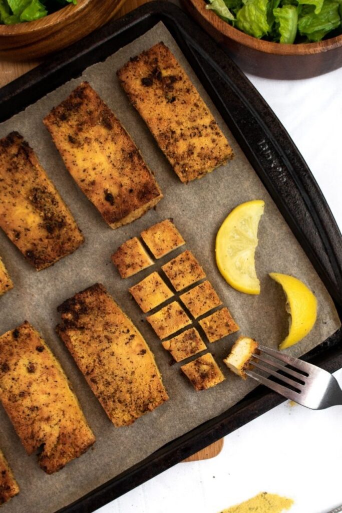 Overhead view of several baked lemon pepper tofu slices on a parchment lined baking sheet cut into small squares