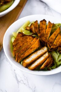 Overhead shot of a chipotle lime tofu cutlet in a bowl on avocado penne pasta