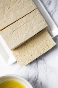 In this post, we'll share how we prepare and cook tofu to taste and FEEL just like chicken! The "Tofu Freezer Trick" is a life-changing method that is a staple in our vegan kitchen. Tofu is frozen and thawed creating a porous meaty texture that will blow your mind. Then, we soak it in a flavorful tofu marinade and slow bake it in the oven until the tofu is crispy on the outside and tender (NOT squishy) on the inside. Use this easy tofu trick to make everything from healthy tofu nuggets, crispy tofu sandwiches, stir fry tofu, and the BEST tofu chicken for salads. We've included 6 of our favorite tofu recipes that use this method to get you started!