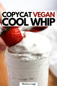 Head on view of a clear glass jar overflowing with vegan cool whip with a strawberry being dipped into the top with text reading copycat vegan cool whip