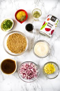 Ingredients needed to make vegan teriyaki burgers: teriyaki sauce, minced red onion, minced garlic, minced ginger, refined coconut oil, a can of beets, TVP, bouillon powder, ground black pepper, scallions, soy sauce, and vital wheat gluten.