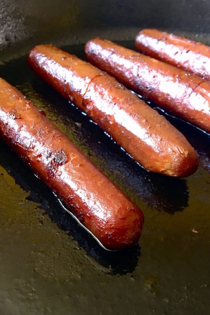 Overhead view of four carrot dogs cooking in a cast iron skillet