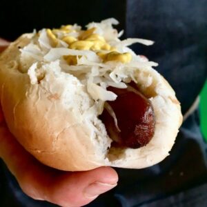 A hand outstretched holding our carrot dog recipe topped with sauerkraut and a drizzle of yellow mustard
