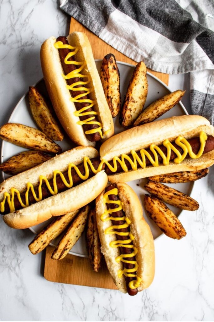 Overhead view of four carrot dogs on a round grey plate topped with mustard and surrounded by french fries