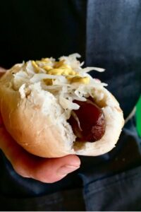 A hand outstretched holding our carrot dog recipe topped with sauerkraut and a drizzle of yellow mustard