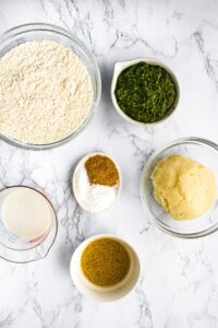 Overhead shot of all the ingredients you need to make vegan potato biscuits with pesto: flour, light brown sugar, salt, baking powder, dairy free pesto, non dairy milk, flax egg, leftover mashed potatoes.