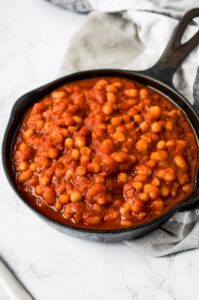 A skillet of healthy vegan baked beans with a black and white checkered napkin on a grey marble background. These easy vegan baked beans are the perfect summer BBQ side dish!