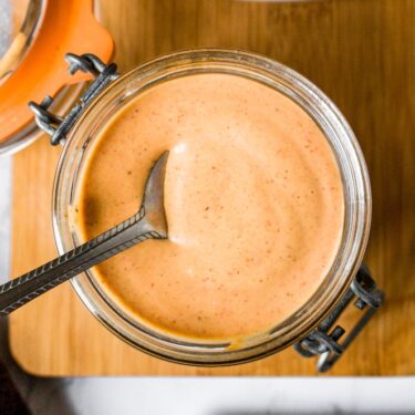 Overhead shot of vegan burger sauce in a jar with a spoon sticking into it. There are french fries and pickles to the side.