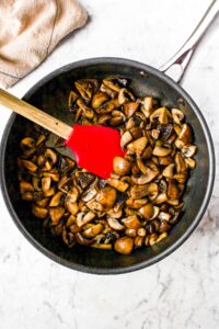 Overhead shot of a non-stick pan filled with freshly sauteed mushrooms with a red rubber spatula pushing them around