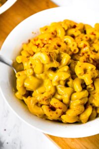 Close-up photo of vegan mac and cheese with sweet potato cheese sauce in a white bowl with a spoon digging into it and smoked paprika sprinkled on top