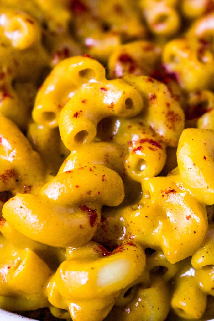 A close-up photo of elbow pasta drenched in dairy free sweet potato cheese sauce and sprinkled with smoked paprika.