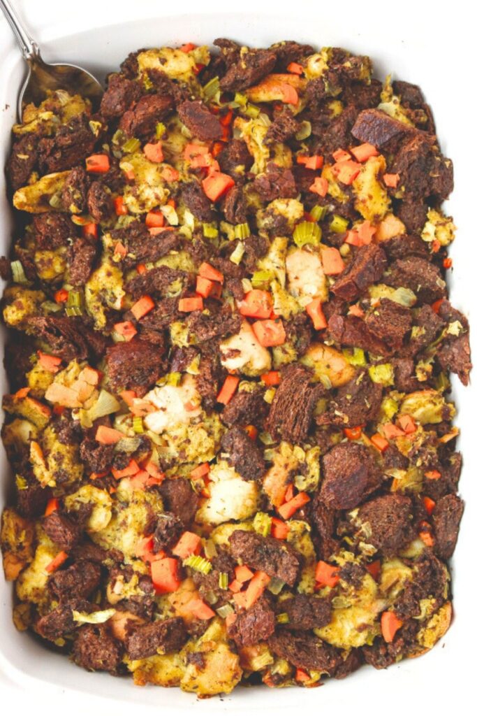Overhead view of a white rectangular casserole dish filled with vegan stuffing with pumpernickel and sourdough bread
