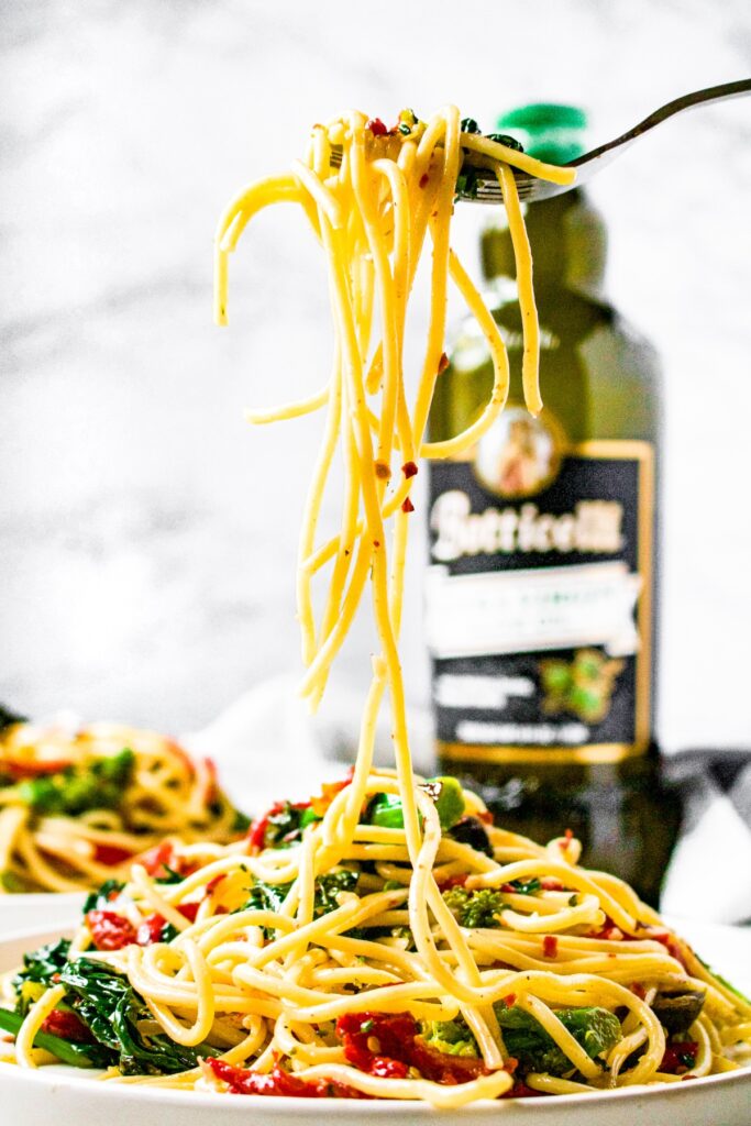 A head-on shot of a fork pulling spaghetti up over a pile of vegetarian aglio e olio with a bottle of Botticelli Extra Virgin Olive Oil in the background.