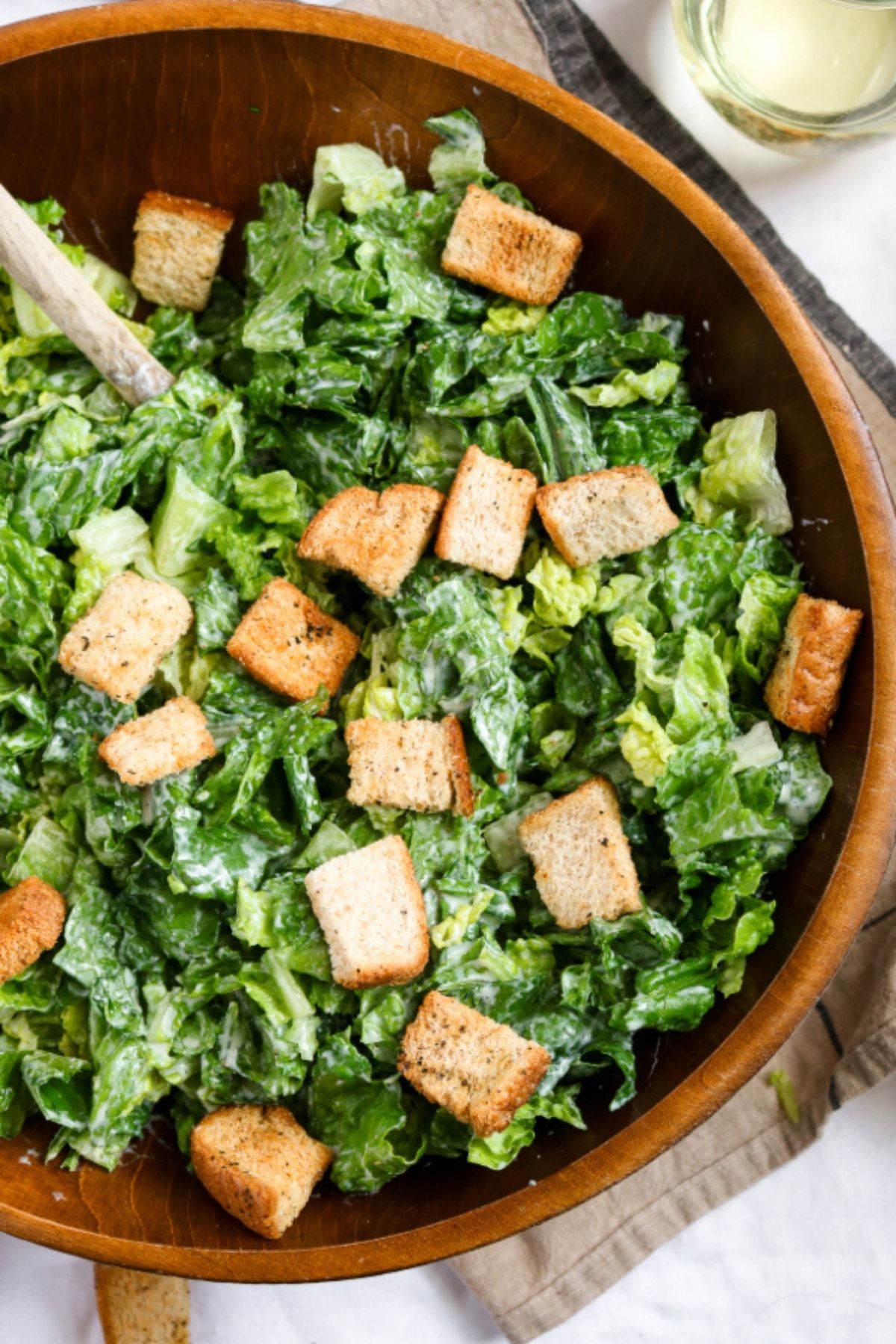 Overhead close up view of a large vegan Caesar salad with croutons in a bamboo salad bowl
