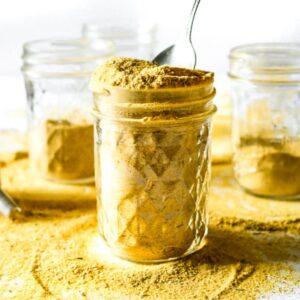 Head on view of a clear glass jar filled with vegan chicken bouillon powder with a spoon sticking into it