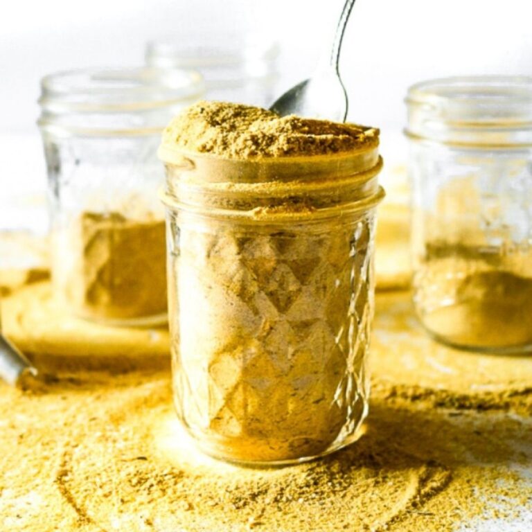 Head on view of a clear glass jar filled with vegan chicken bouillon powder with a spoon sticking into it