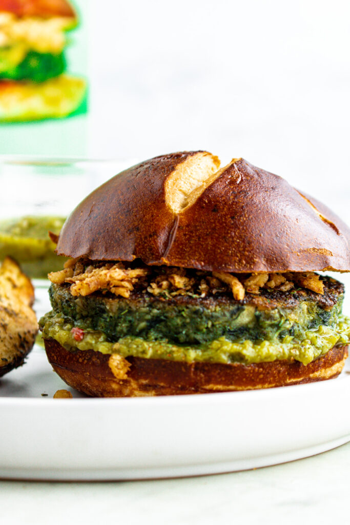 Head-on view of a green veggie burger on a pretzel bun topped with crispy onions