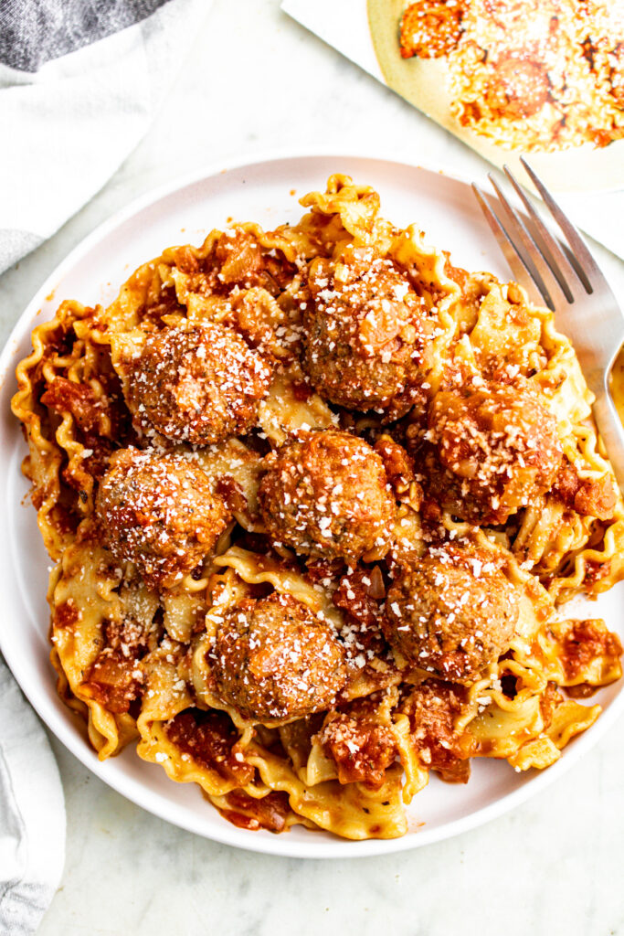 Overhead view of a round white plate piled high with malfaldine pasta topped with vegan meatballs