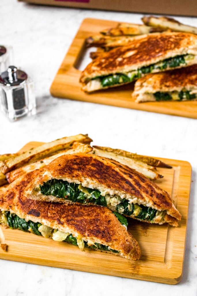 Close up shot of a plant based spinach artichoke grilled cheese next to a pile of oregano fries