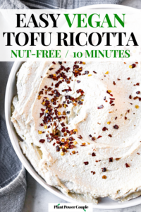 Close up overhead shot of a circular schmear of dairy-free ricotta on a round white plate sprinkled with red pepper flakes. Text reads: easy vegan tofu ricotta, nut-free / 10-minutes