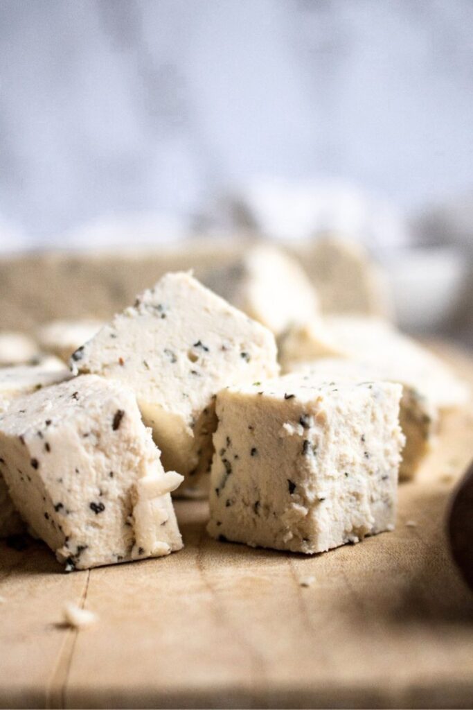 Close up head on photo of a pile of half a dozen vegan feta cubes on a wood cutting board