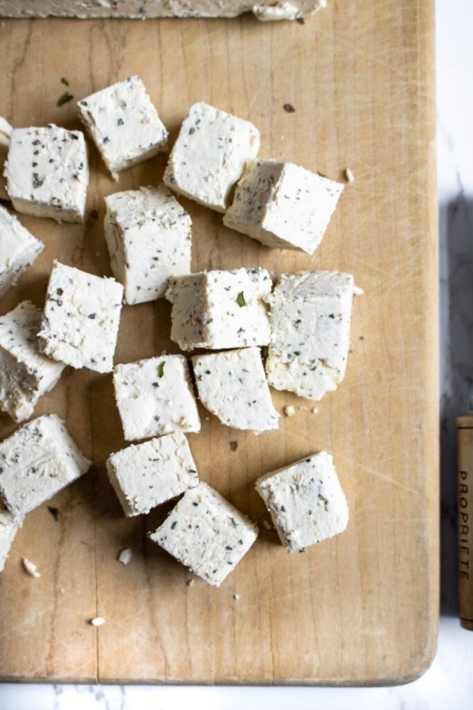Overhead view of a pile of vegan feta cubes on a wood cutting board