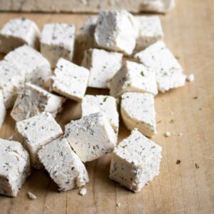 Overhead view of a pile of vegan feta cubes on a wood cutting board