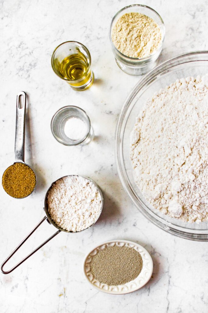 Overhead shot of the ingredients you need to make a fluffy homemade pizza dough: all purpose flour, active dry yeast, light brown sugar, vital wheat gluten, and olive oil.