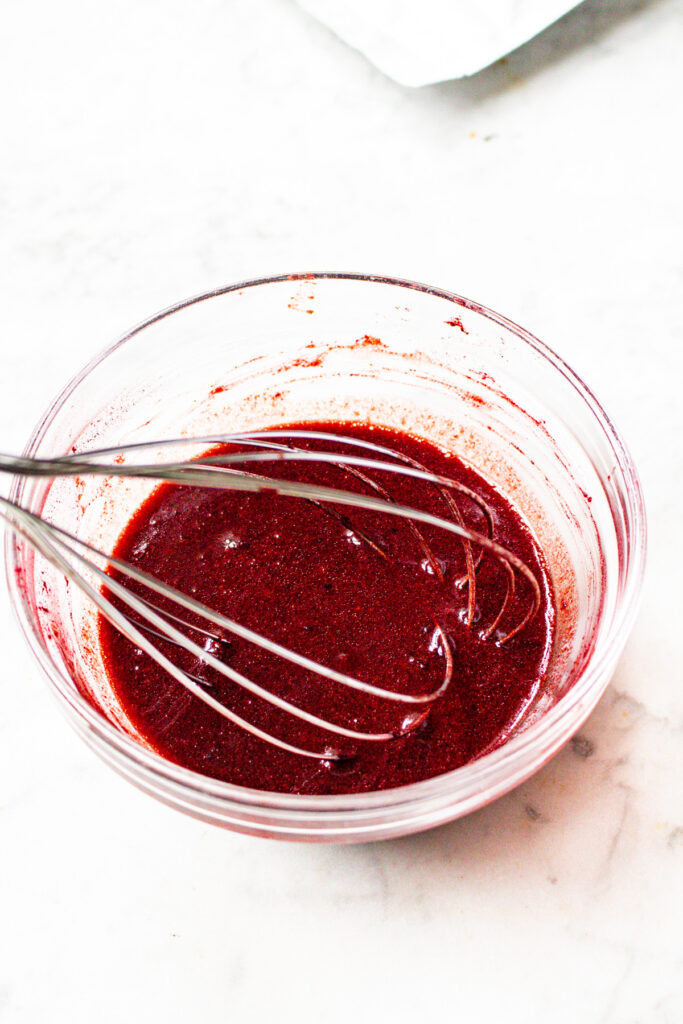 Overhead view of a whisk mixing marinade for rice paper bacon with a vibrant pink color