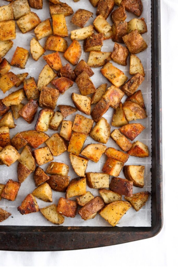 Overhead view of a parchment lined baking sheet with vegan roast potatoes scattered on top