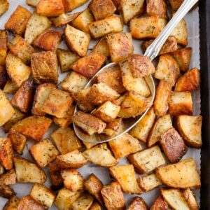Overhead close up view of easy roasted potatoes scattered on a parchment-lined baking sheet with a big spoon digging into them