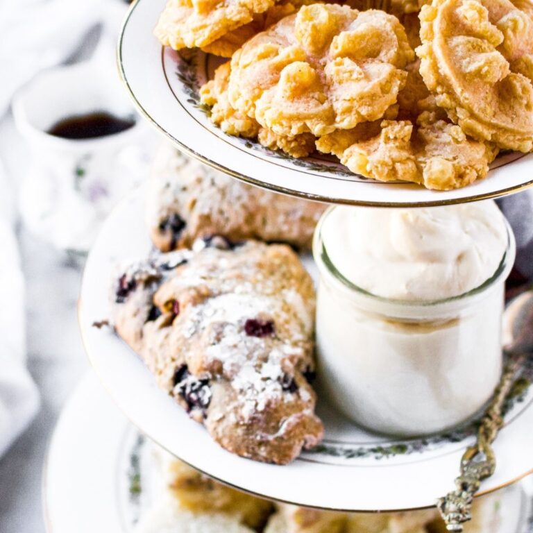 Overhead photo of a 3-tier tea tray with various vegan afternoon tea recipes like finger sandwiches, blueberry scones and vegan clotted cream, and dairy free cheese straws