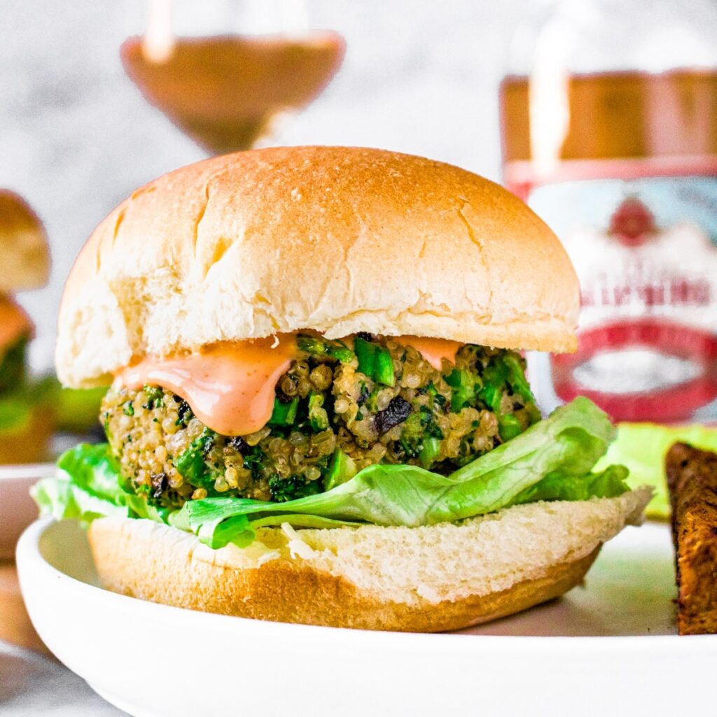 Head on view of a mushroom quinoa burger on a bun with sriracha aioli dripping down the side. A bottle and glass of French rose is in the background.