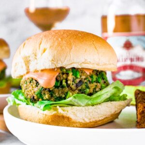 Head on view of a mushroom quinoa burger on a bun with sriracha aioli dripping down the side. A bottle and glass of French rose is in the background.