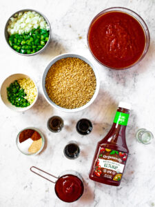Overhead shot of ingredients in vegan sloppy joes: TVP, ketchup, canned diced tomatoes, green peppers, onion, garlic, jalapeno, chili powder, garlic powder, vegan worcestershire, soy sauce, gravy master, salt, and pepper
