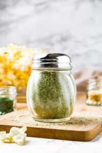 A head-on shot of vegan ranch seasoning in a classic restaurant shaker jar with a metal lid. There is a bowl of popcorn behind the jar.