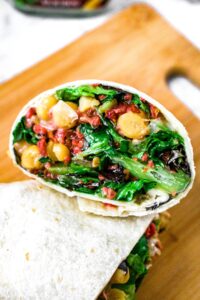 Overhead close up shot of a vegetarian and vegan wrap with chickpeas, dairy free ranch, greens, imitation bacon bits, and sun-dried tomatoes.